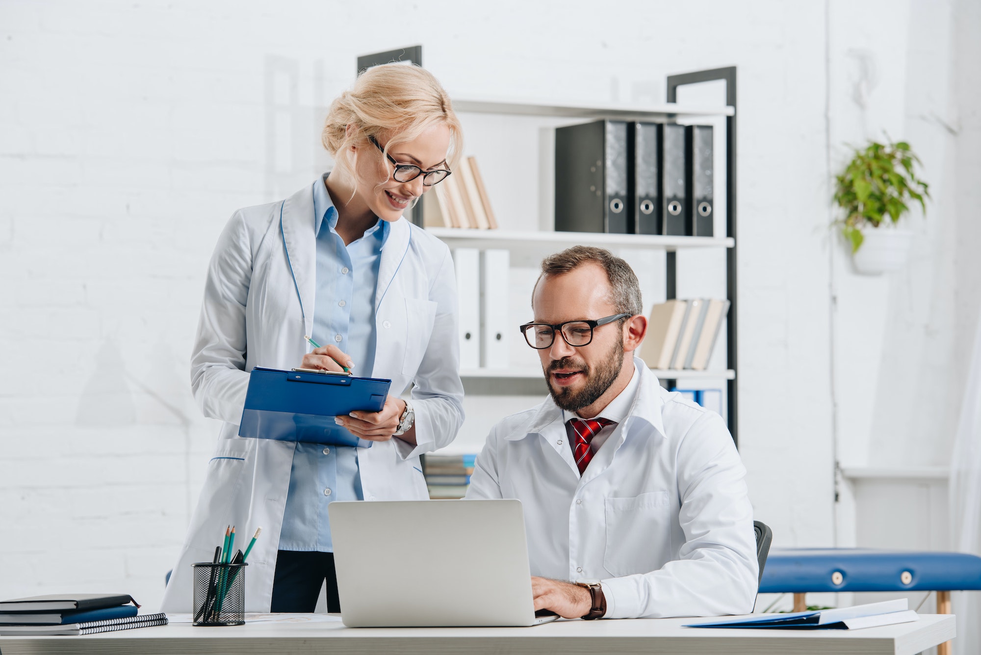 portrait of physiotherapists in white coats and eyeglasses working together in clinic